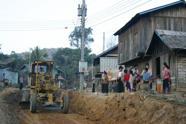 Project Phongsali 2011: Equipment rumbles through town known to have bombs.  Children dig in uncleared soil.